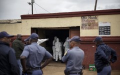 Police officers watch as SAPS Forensic Pathology Services members work at the scene of the Bekkersdal tavern attack. AFP/Emmanuel Croset