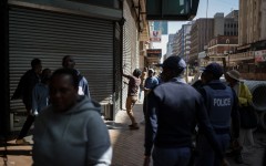 South African Police Service (SAPS) officers watch as a worker closes the shutters of a shop while protestors pass by during a protest march against undocumented migrants organised by “March and March” in Johannesburg on April 29, 2026. 