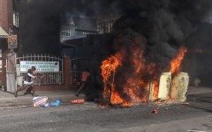 Protesters take cover past a burning car after clashes erupted between protesters and foreign nationals in Durban on October 8, 2026.