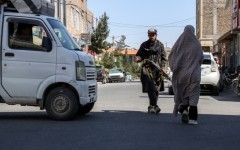 An Afghan burqa-clad woman walks past a Taliban security personnel standing guard outside a mosque in Shahrak-e-Almahdi, Jebrail district of Herat Province on June 11, 2026