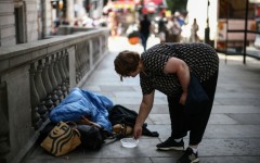 A woman puts some coins in a dish next to a man wrapped up with his dog on a London street