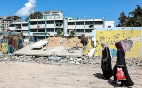 Women walk past the destroyed wall of a school for boys run by the UN agency for Palestinian refugees (UNRWA)