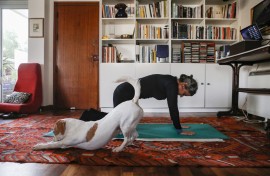 Thanks to an online pilates course, a Cypriot woman exercises at home, while her dog stretches too beside her.