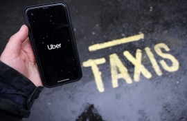 File: A man poses holding a smartphone showing the App for ride-sharing service Uber. AFP/Tolga Akmen