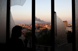 A Palestinian child watches as smoke billows on the horizon after an Israeli air strike in Gaza City on October 13, 2023. 