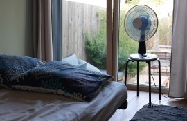 File: A fan next to a bed in a room. 