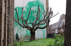 A stencil of a person having spray painted tree foliage onto a wall behind a leafless tree, a graffiti artwork confirmed as being the work of Banksy. AFP/Adrian Dennis