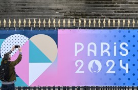 A bystander uses a smartphone to take an image of a banner for the forthcoming Paris 2024 Olympic Games. AFP/Stefano Rellandini