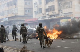 Anti-riot police officers with their dogs walk down Eduardo Mondlane Avenue past burning barricades made by protesters in Maputo. AFP/Alfredo Zuniga