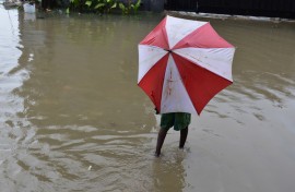 A person with an umbrella walking in a flooded road. GettyImages/onyebuchi ugwumbah