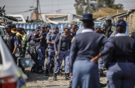 South African Police Service (SAPS) officers walk during raid to retrieve looted goods during a protest at Diepkloof Hostel in Soweto on May 19, 2025. 