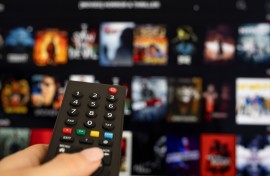 File: A woman holding a TV remote with streaming services in the background. GettyImages/bymuratdeniz