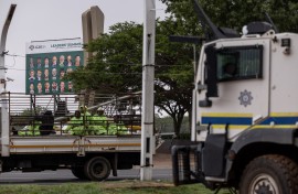 A truck transporting workers drives past a SAPS armoured vehicle outside the Nasrec Expo Centre in Johannesburg. AFP/Emmanuel Croset 