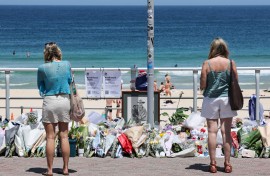 People stand in front floral tributes left at the promenade of Bondi Beach in Sydney. AFP/David Gray