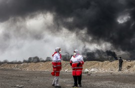 Members of Iran's Red Crescent society stand near smoke plumes from an ongoing fire following an overnight airstrike on the Shahran oil refinery in northwestern Tehran. AFP