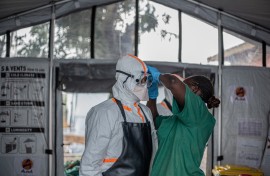 A hygiene worker helps a doctor put on personal protective equipment (PPE) before entering the Rwampara Ebola Treatment Centre. AFP/Benediction Murhabazi
