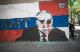 A woman walks past a vandalised mural of Russian President Vladimir Putin in Belgrade