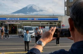 Tourists take pictures of Mount Fuji from opposite a convenience store in the town of Fujikawaguchiko, Yamanashi prefecture