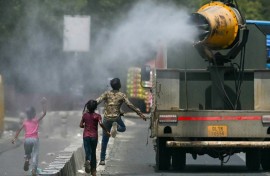 Children run behind a truck spraying water along a street on a hot summer day in New Delhi on Tuesday