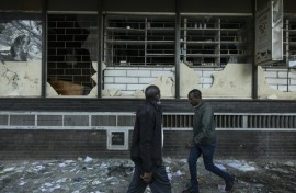 Pedestrians walk past damaged shops vandalised  during the deadly violence which rocked Nairobi over proposed tax hikes