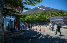 The summit of Mount Fuji is seen as people gather in front of the restaurant and shopping area of the Fuji Subaru Line 5th station, which leads to the popular Yoshida trail for hikers -- new rules will be in effect this season to combat overcrowding