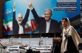 A woman walks past a picture of Iranian President Masoud Pezeshkian (R) and slain Hamas leader Ismail Haniyeh in Tehran
