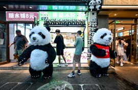 Men wearing panda costumes stand outside food stalls in Beijing in July 2024