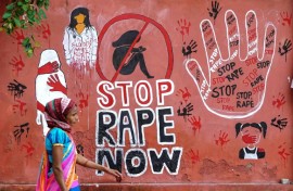 A woman walks past a mural painted on a wall in Ajmer condemning the rape and murder of a doctor in India's West Bengal state