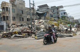 People ride a motorbike past damaged buildings in Mandalay, Myanmar