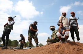 Tribal fighters stand next to a government checkpoint east of Sweida city, in southern Syria