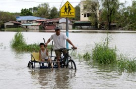 A father and child ride a tricycle through a flooded street in a village north of Manila on Friday