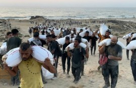 Palestinians carry bags of flour from aid convoys in the Israeli-controlled Zikim border crossing in the northern Gaza Strip