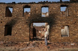 A man stands in front of a ruined burnt house after a wildfire in the village of Castrocalbon, northwestern Spain