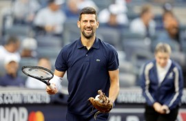 Tennis star Novak Djokovic carries his racquet to the mound before throwing the ceremonial first pitch at a New York Yankees baseball game