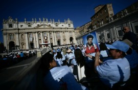A faithful holds a portrait of late teenager Carlo Acutis in front of Saint Peter's