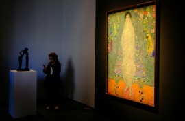 The piece represents the daughter of Klimt's main patron dressed in a white imperial Chinese dress, standing before a blue tapestry with Asian-inspired motifs