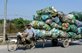 Men on a motorbike pull a cart carrying plastic waste on the outskirts of Hanoi