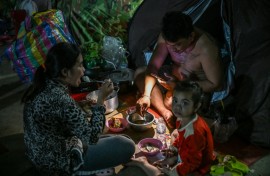 A displaced family uses a flashlight as they eat a meal at a temporary camp in Banteay Meanchey province on December 12, 2025, amid clashes along the Cambodia-Thailand border