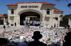 Mourners stand near tributes piled together at the front of the Bondi Pavilion, in memory of the victims of the Bondi Beach shooting