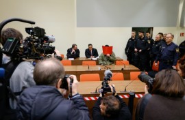 The defendant, partially identified as Farhad N., hides his face behind a folder at the start of his trial in Munich