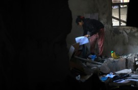 A Palestinian girl picks up her school work from the debris of a destroyed house