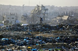A Palestinian boy searches for recyclable material at a landfill against the backdrop of destroyed buildings in Khan Yunis, in the southern Gaza Strip