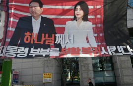 A man walks past a banner showing a picture of South Korea's former impeached president Yoon Suk Yeol and his wife Kim Keon Hee