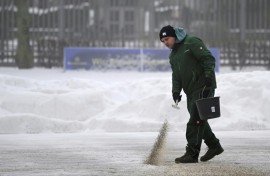 A man spreads granules on a snow-covered surface in front of the defence ministry in Berlin