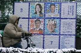 A person rides past a board displaying posters of candidates for the Lower House election on February 8, 2026