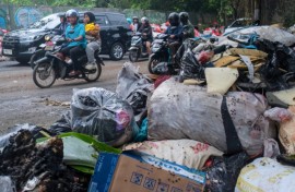 Vehicles driving along a road littered with illegally dumped waste in Pamulang, South Tangerang, Banten