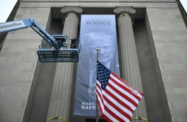 Workers on an aerial lift watch after installing a new banner featuring an image of US President Donald Trump on the facade of the US Department of Justice headquarters building in Washington, DC
