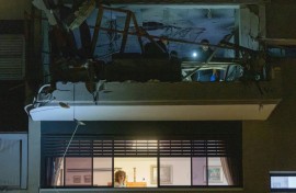 A woman stands at a window as first responders and security forces inspect a damaged apartment above after the building was hit by an Iranian missile strike in Ramat Gan, on the outskirts of Tel Aviv, early on March 18, 2026