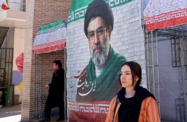 A woman walks past a large tiled image of Iran's current leader Ayatollah Mojtaba Khamenei outside a metro station in Tehran