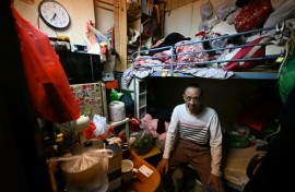 Guan Ci sits on his bed in his subdivided housing unit in Kowloon, Hong Kong